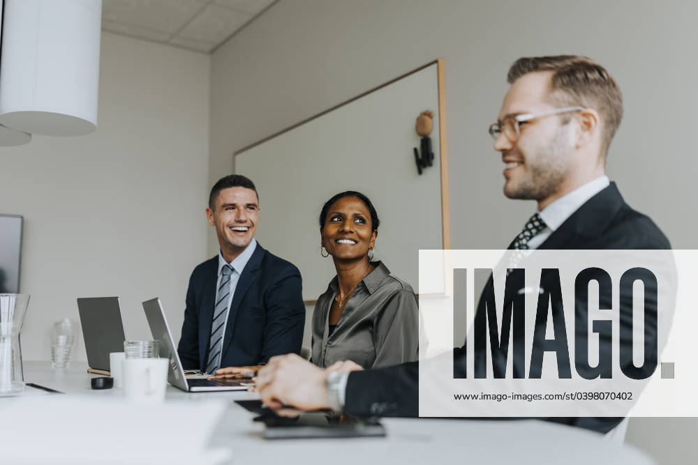 Smiling colleagues looking at businessman while sitting in board room Sweden, Gothenburg, model released, property released