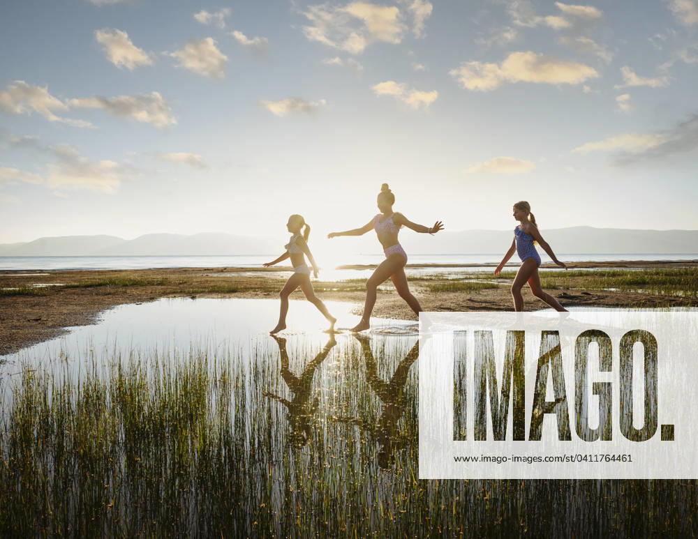 Girls (10-11, 12-13, 14-15) walking on stepping stones in lake at sunrise , 20.12.2023, model released, TTBB_ti0007_02293.jpg, Pre-Adolescent Child,Girls,10-11 Years,12-13 Years,Teenager,Teenage Girls,14-15 Years,Outdoors,Sunrise,Horizontal,Arms Raised,Walking,Sister,Family,Sun,Sunlight,Clear Sky,Summer,Landscape,Scenics,Tranquility,Lake,Lakeshore,Vacations,Vitality,Reeds,Back Li