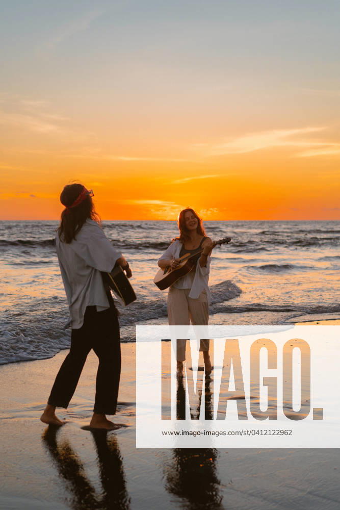 IMAGO Creative, Jahreszeit Sommer, Sommerferien Women friends play guitars on the beach. Sunset on the ocean. Bali Kuta, Bali, Indonesia CR_YUKI240206-1331712-01 ,model released, Symbolfoto ,property released