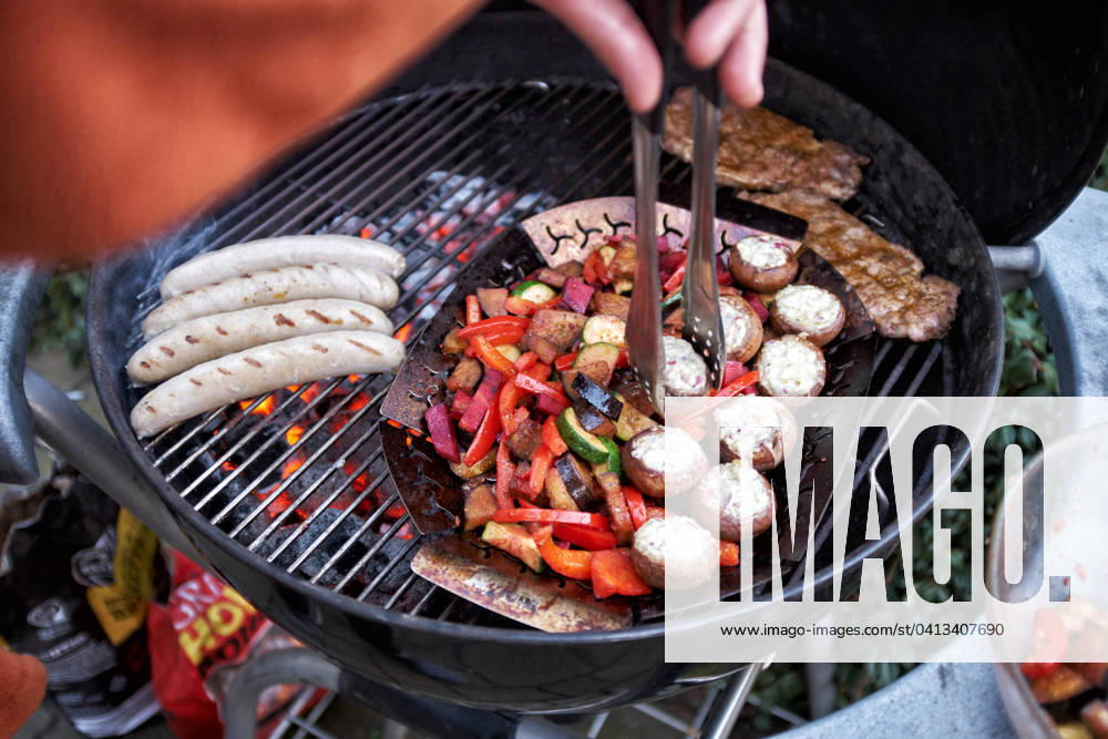 Grillen Auf einem Rundgrill werden gleichzeitig Wuerstchen, Steaks und Gemuese gegrillt. Essen NRW