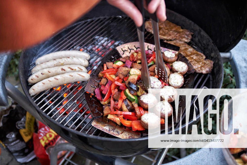 Grillen Auf einem Rundgrill werden gleichzeitig Wuerstchen, Steaks und Gemuese gegrillt. Essen NRW