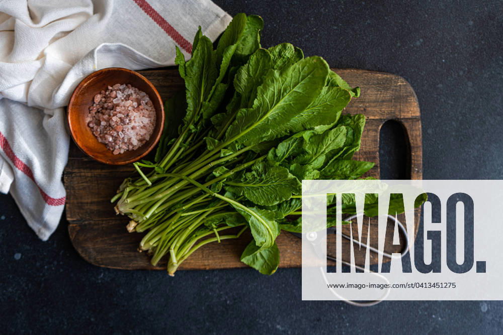 IMAGO Creative, Food, Trend, Meal Prep Top view of bunch of fresh arugula leaves alongside a bowl of pink salt and scissors on a rustic wooden cutting board, set against a dark tabletop with a striped towel Model Released AnnaBogush_ID18975_564904_007