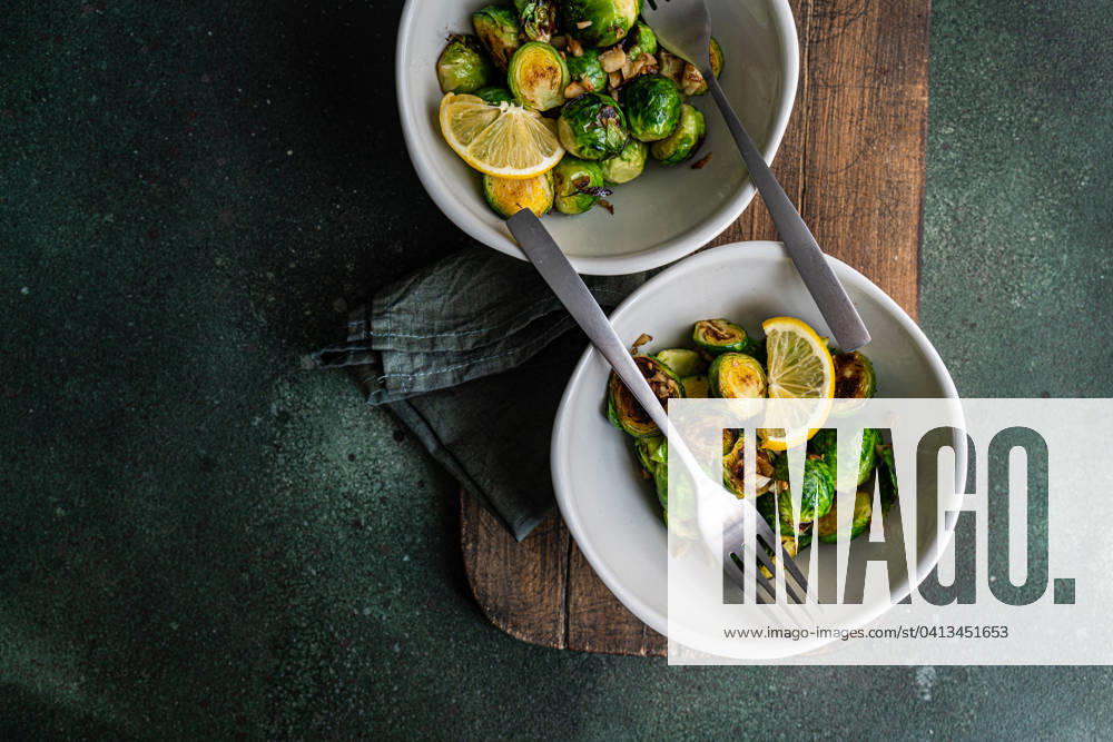 Top view of bowl of grilled Brussels sprouts seasoned with garlic and spices, garnished with a slice of lemon, served on a wooden board with a fork Model Released AnnaBogush_ID19160_569963_006