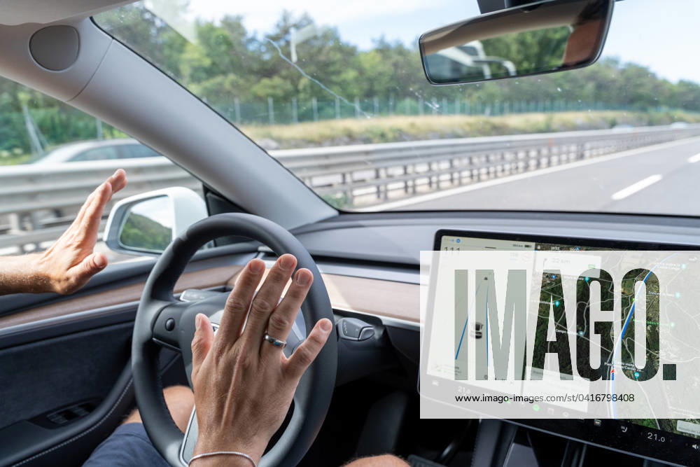 Mann fährt mit dem Tesla Model Y Auto auf der Autobahn mit Autopilot ohne Hände am Lenkrad