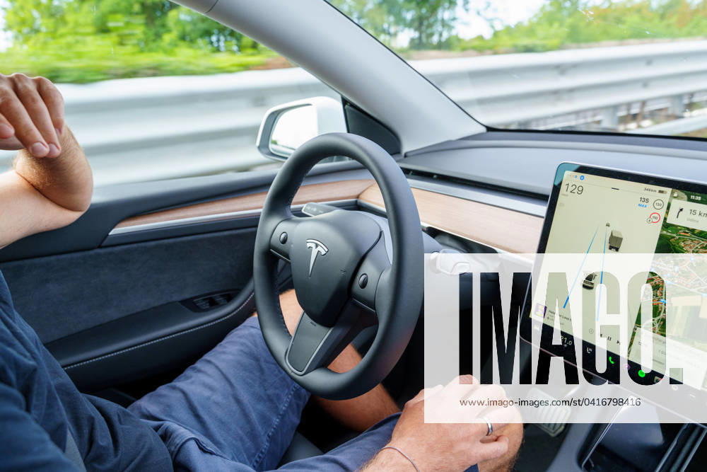 Mann fährt mit dem Tesla Model Y Auto auf der Autobahn mit Autopilot ohne Hände am Lenkrad