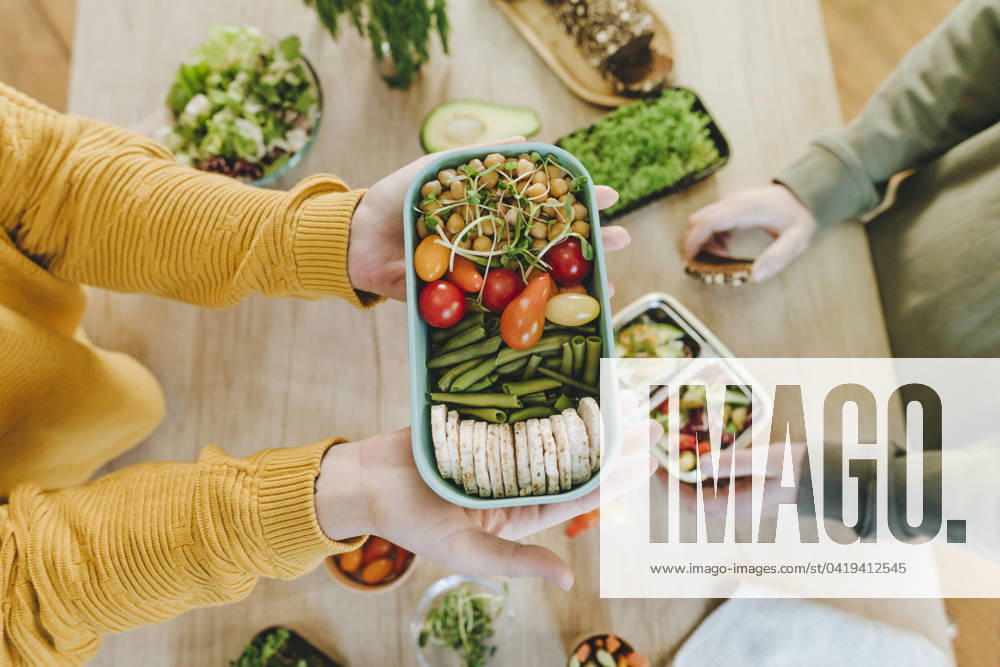 IMAGO Creative, Food, Trend, Meal Prep Hands of woman holding vegetarian food lunch box near man at table model released, Symbolfoto property released, YTF01686