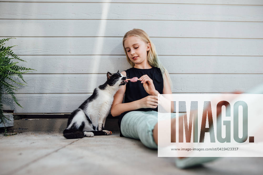 IMAGO Creative, Jahreszeit Sommer, Hitze Wide shot of preteen girl holding popsicle for cat to lick. Bismarck, North Dakota, United States CR_KIFR240228-1358214-01 ,model released, Symbolfoto