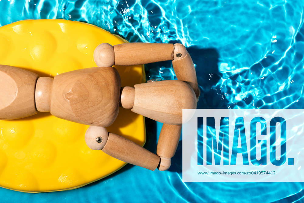 Wooden artist s mannequin relaxing on a yellow pool float in clear blue swimming pool water, simulating a summer leisure scene Model Released SergioVictorVega_ID19896_589862_003