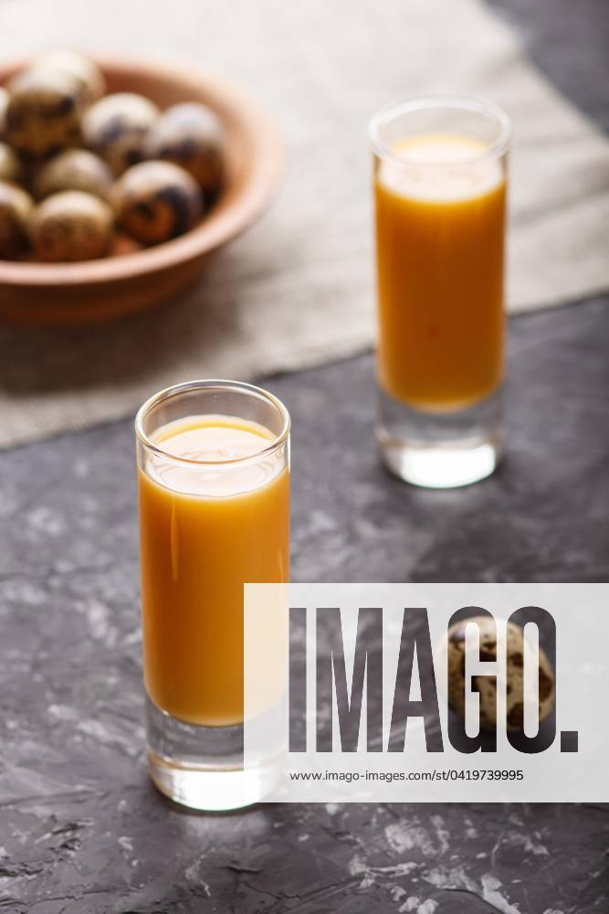 Süßer Eierlikör im Glas mit Wachteleiern auf einem schwarzen Betonhintergrund. Seitenansicht, unauffällig, Nahaufnahme