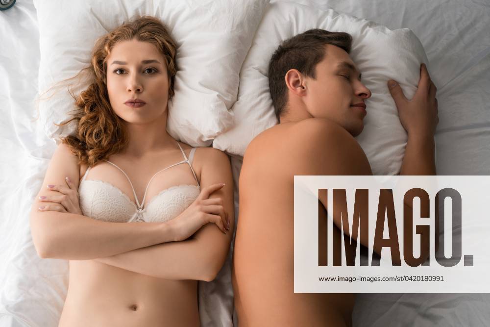 Unsatisfied woman in lingerie lying on bed with sleeping man Top view of discontent female in underwear lying with crossed arms on bed next to sleeping boyfriend ,model released, Symbolfoto