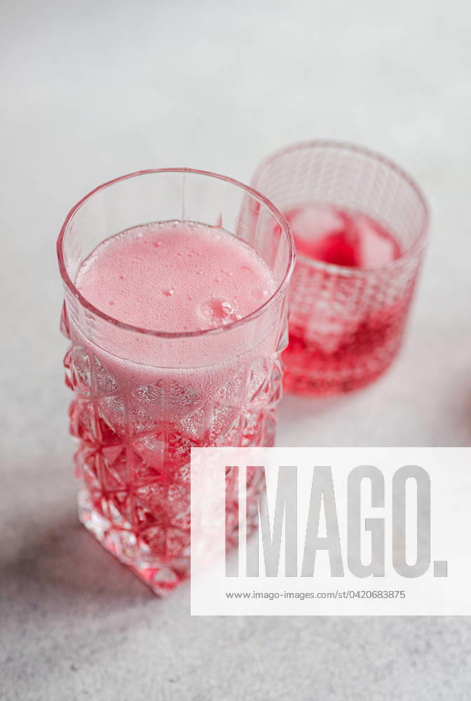 Two textured glasses featuring a refreshing cherry vodka and tonic cocktail with effervescent bubbles and ice cubes, against a soft background. Model Released AnnaBogush_ID19984_591792_001