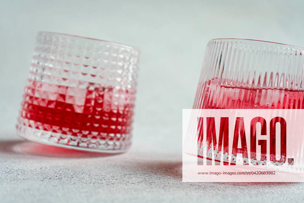 Two textured glasses filled with ice and a vibrant cherry vodka and tonic cocktail, cast on a simple backdrop. Model Released AnnaBogush_ID19984_591799_005