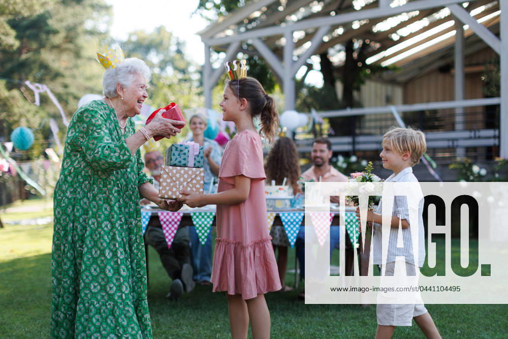 Garden birthday party for senior lady. Beautiful senior birthday woman receiving gift from grandchildren. Garden birthday party for senior lady. Beautiful senior birthday woman receiving gift and flowers from grandchildren. model released