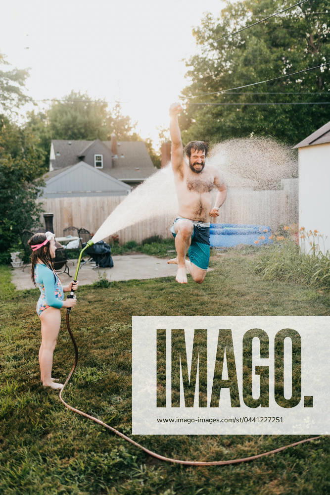 Young girl holds garden hose while dad runs through water Sioux Falls, South Dakota, United States CR_ASWE240317-1369125-01 ,model released, Symbolfoto ,property released