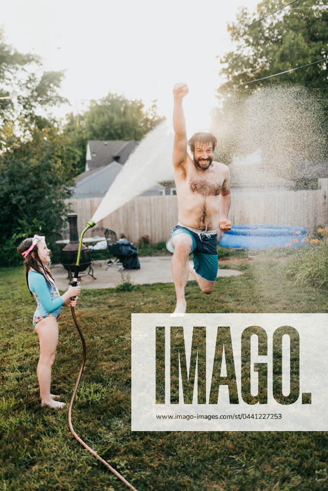 Young girl holds garden hose while dad runs through water Sioux Falls, South Dakota, United States CR_ASWE240317-1369126-01 ,model released, Symbolfoto ,property released