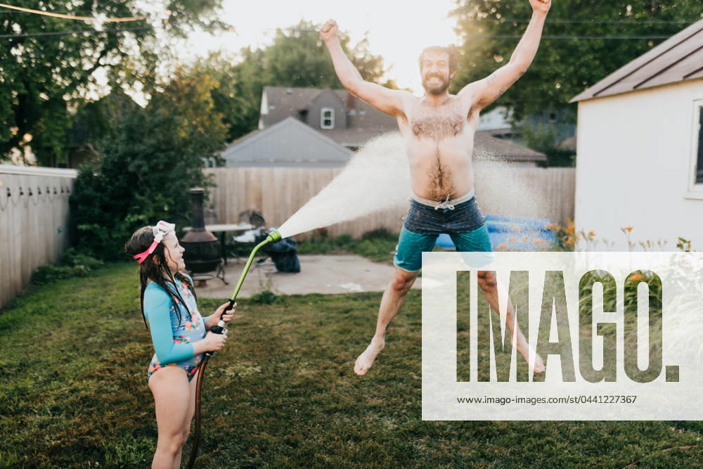 Young girl holds garden hose while dad runs through water Sioux Falls, South Dakota, United States CR_ASWE240317-1369151-01 ,model released, Symbolfoto ,property released