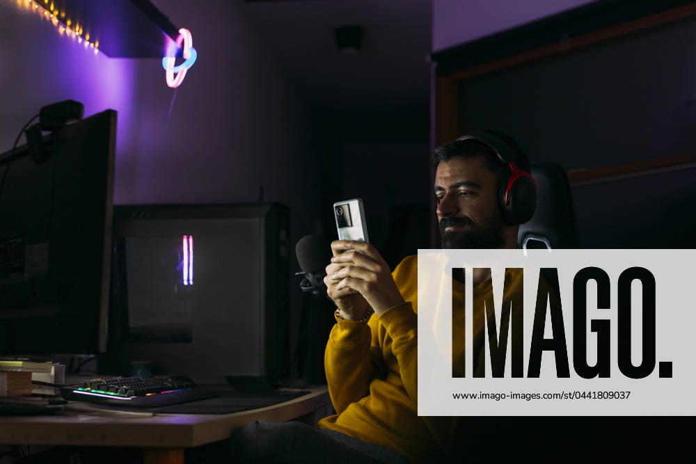 IMAGO Creative, Lifestyle, Gaming Influencer using smart phone near desktop PC at home model released, Symbolfoto property released, EGHF00828