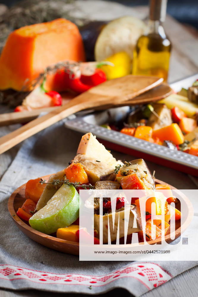 Mixed roasted vegetables with thyme in a tray and wooden plate. Selective focus.