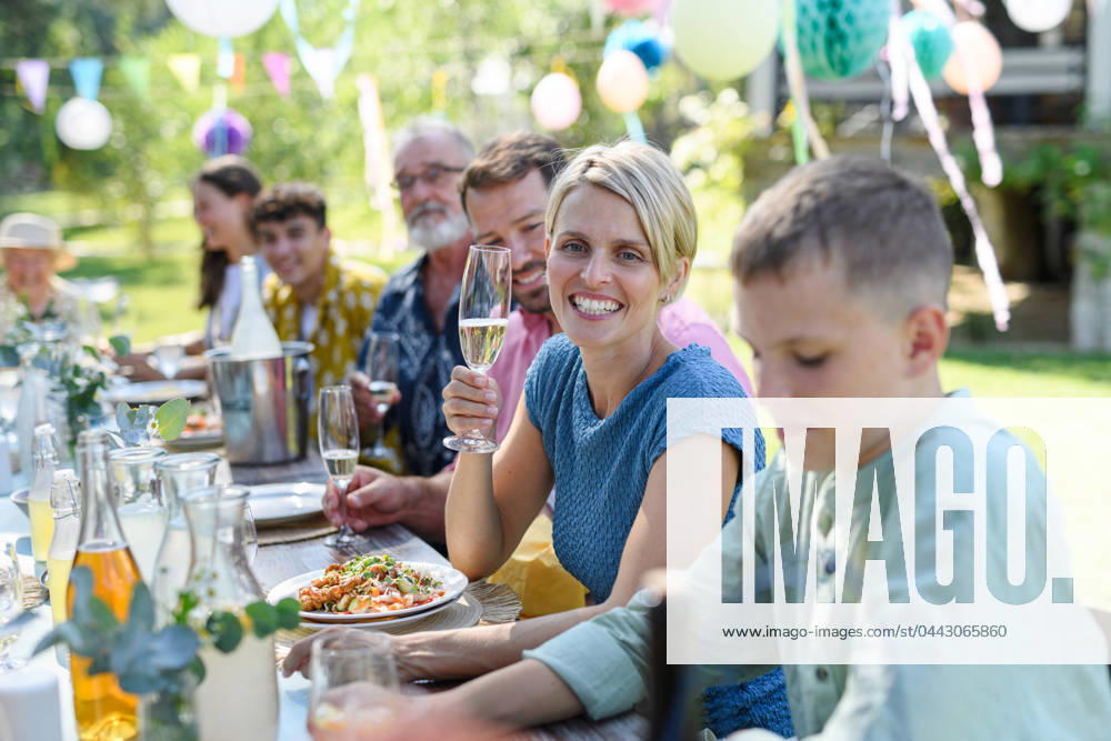 Family chatting, and having fun at party table during summer garden party. Beautiful woman cheering with glass with champagne. Family chatting, and having fun at party table during summer garden party. Beautiful woman toasting, cheering with glass with champagne. model released