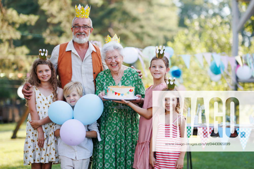 Garden birthday party for senior lady. Beautiful senior birthday woman holding cake and posing for pohoto with grandchildren and husband. Garden birthday party for senior lady. Beautiful senior birthday woman holding cake and posing for pohoto with grandchildren and husband. Birthday celebration with paper crowns. model released