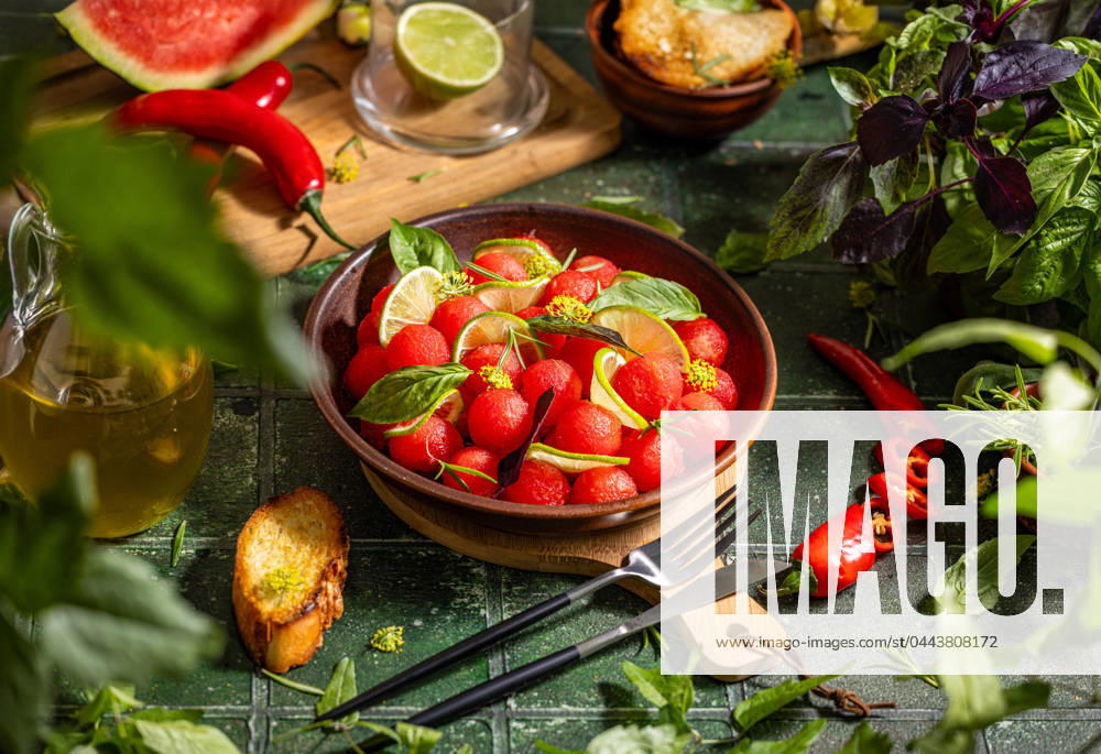 Spicy salad of fresh watermelon balls with basil, lime, rosemary and fennel, topping with olive oil Spicy salad of fresh watermelon balls with basil, lime, rosemary and fennel, topping with olive oil on dark green table surface with sunny light