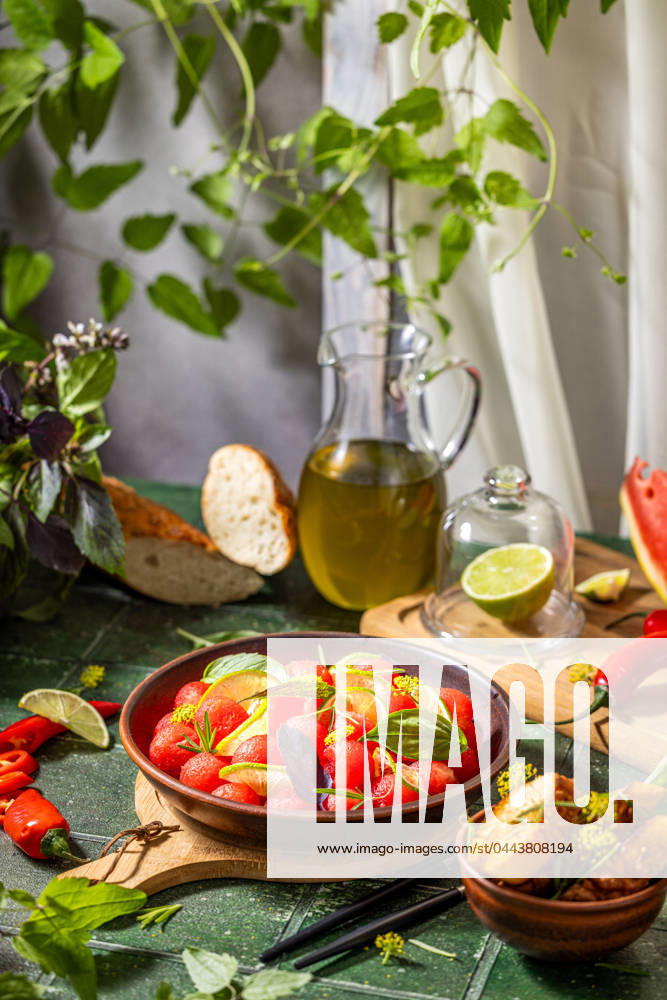 Spicy salad of fresh watermelon balls with basil, lime, rosemary and fennel, topping with olive oil Spicy salad of fresh watermelon balls with basil, lime, rosemary and fennel, topping with olive oil on dark green table surface with sunny light