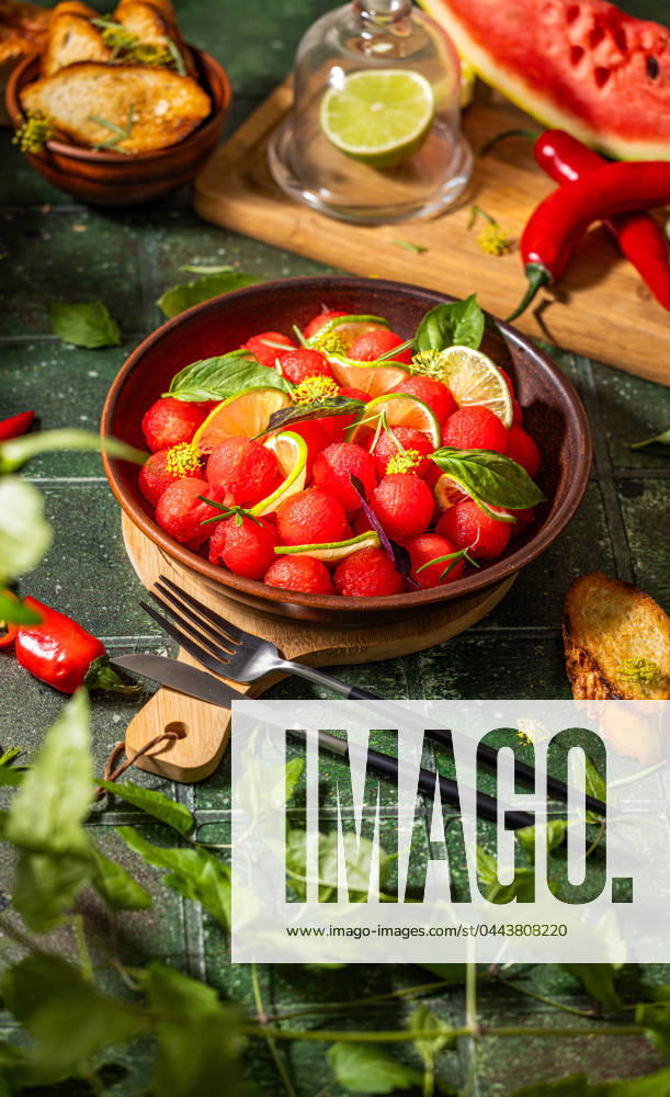 Spicy salad of fresh watermelon balls with basil, lime, rosemary and fennel, topping with olive oil Spicy salad of fresh watermelon balls with basil, lime, rosemary and fennel, topping with olive oil on dark green table surface with sunny light