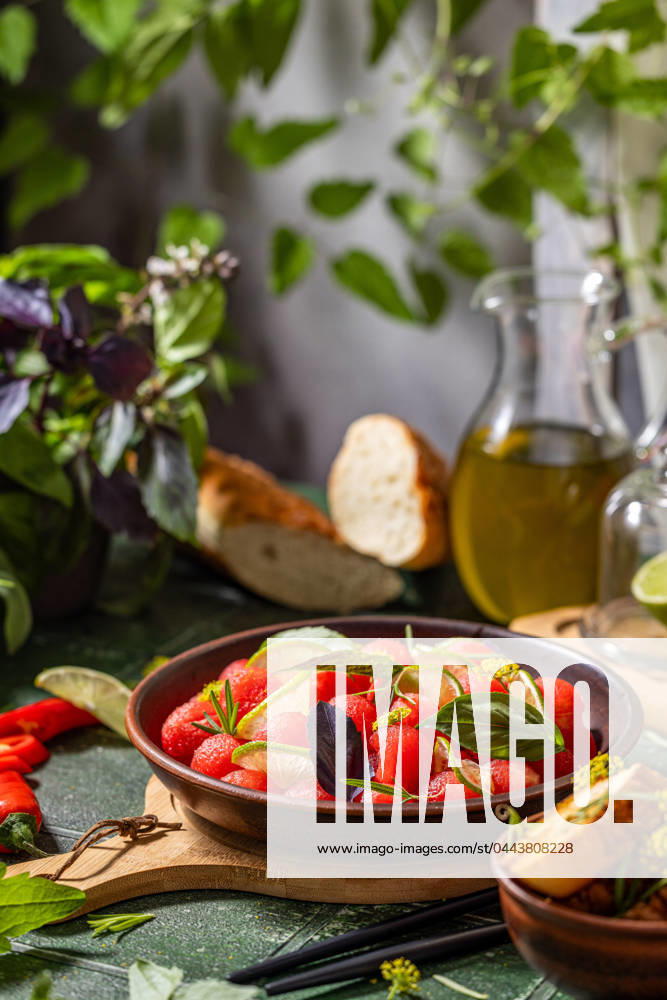 Spicy salad of fresh watermelon balls with basil, lime, rosemary and fennel, topping with olive oil Spicy salad of fresh watermelon balls with basil, lime, rosemary and fennel, topping with olive oil on dark green table surface with sunny light