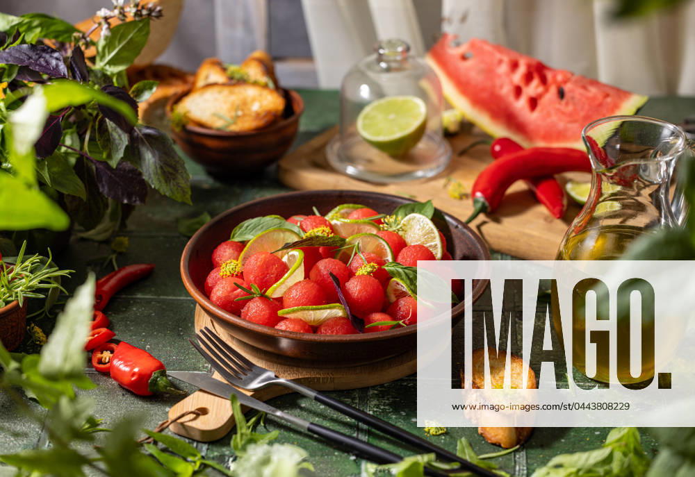 Spicy salad of fresh watermelon balls with basil, lime, rosemary and fennel, topping with olive oil Spicy salad of fresh watermelon balls with basil, lime, rosemary and fennel, topping with olive oil on dark green table surface with sunny light