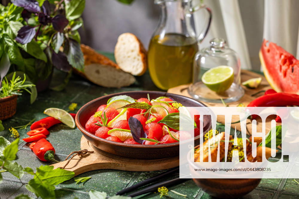 Spicy salad of fresh watermelon balls with basil, lime, rosemary and fennel, topping with olive oil Spicy salad of fresh watermelon balls with basil, lime, rosemary and fennel, topping with olive oil on dark green table surface with sunny light
