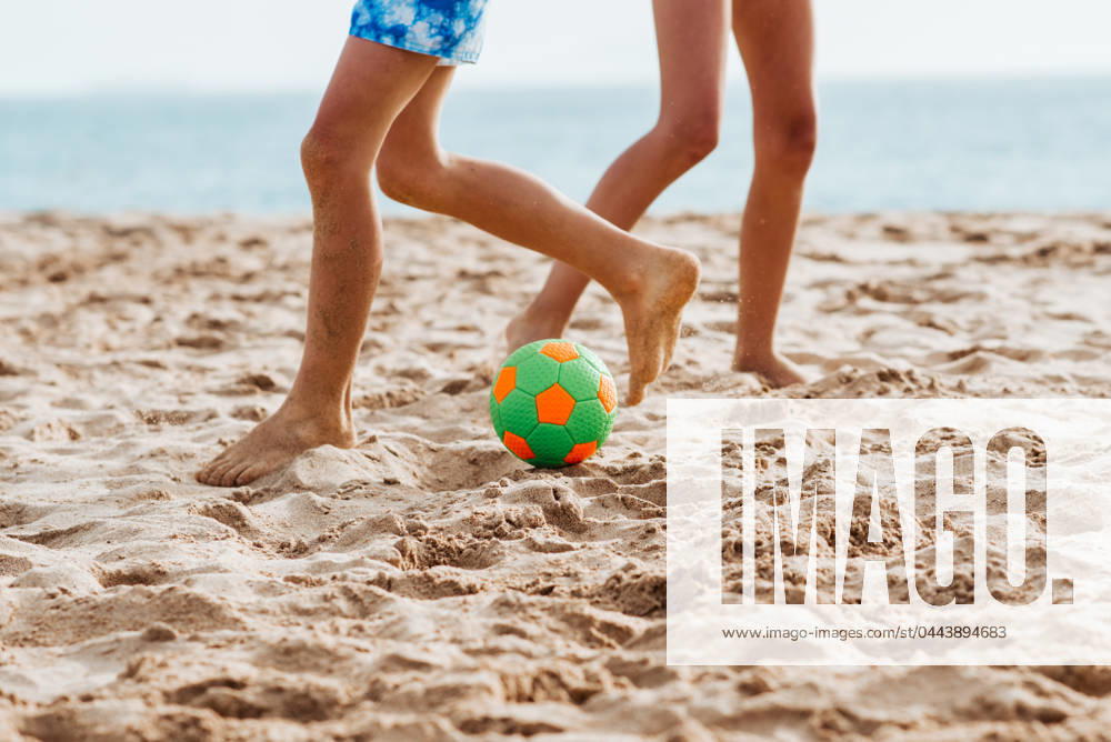 Siblings playing on beach with ball, playing football. Concept of family beach summer vacation with kids. Siblings playing on beach with ball, playing football. Concept of family beach summer vacation with kids. Close up on legs. model released