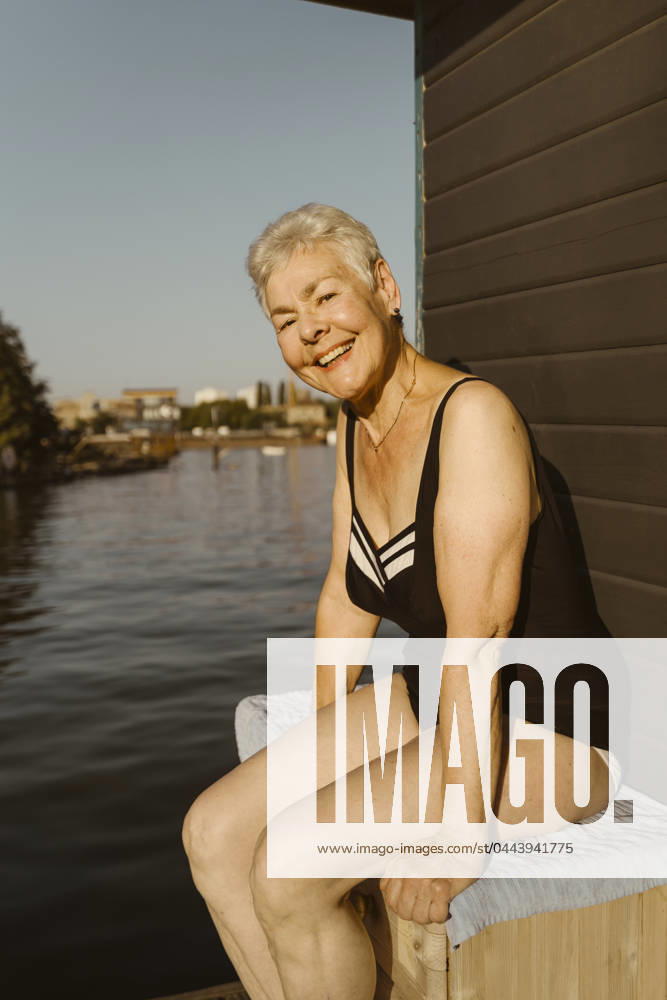 Portrait of happy senior woman wearing swimsuit while sitting near lake on houseboat Germany, Berlin, model released, property released