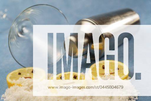 Lemon slices with cloves and cinnamon forming a smiley face on a pile of salt next to a cocktail shaker and a crystal glass with blue background 23592764 RECORD DATE NOT STATED