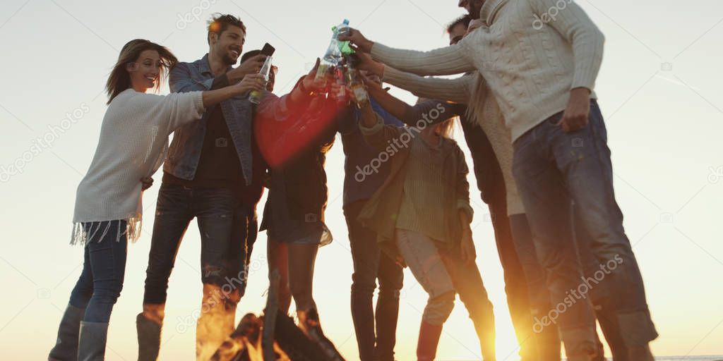 Young Friends Making A Toast With Beer and having fun Around Campfire at beach party on autumn day model released