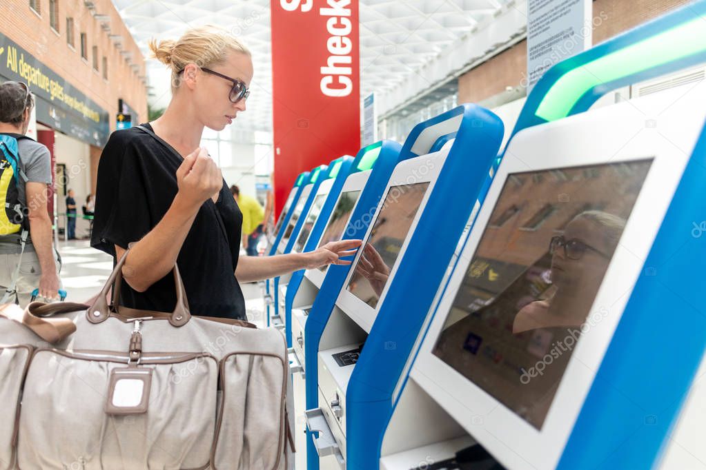 Casual caucasian woman using smart phone application and check-in machine at the airport getting the boarding pass. Modern technology on airport. model released