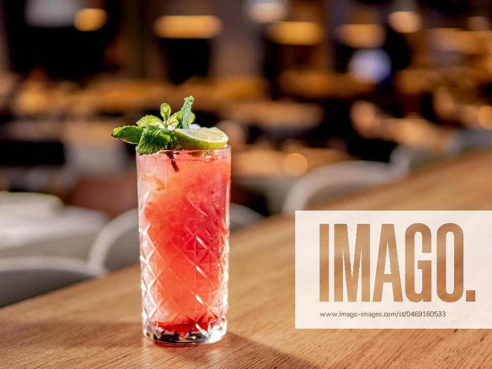 Red pink cocktail with lime and mint in restaurant Red non-alcohol cocktail with crushed ice in glass on wooden bar counter in restaurant interior. Gin alcohol cocktail decorated lime and mint. Pink cold alcoholic cocktail in bar or nightclub background. Copy space
