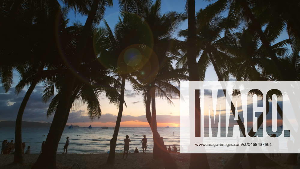 Sunset on beach with people and palms Silhouetted people and palms near sea. Sunset at tropical White beach, Boracay island, Philippines