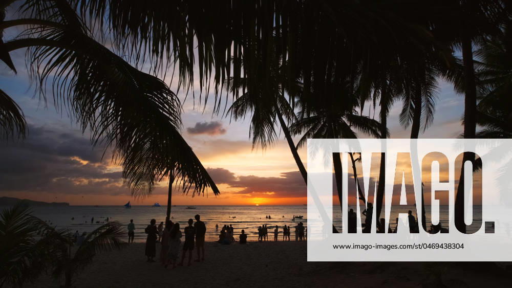 Sunset on beach with people and palms Silhouetted people and palms near sea. Sunset at tropical White beach, Boracay island, Philippines