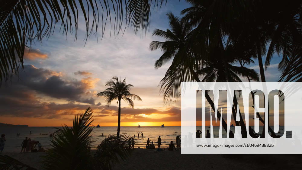 Sunset on beach with people and palms Silhouetted people and palms near sea. Sunset at tropical White beach, Boracay island, Philippines