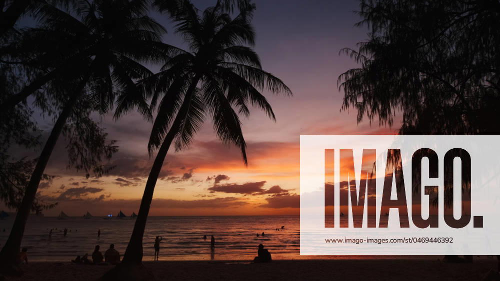 Sunset on beach with people and palms Silhouetted people and palms near sea. Sunset at tropical White beach, Boracay island, Philippines