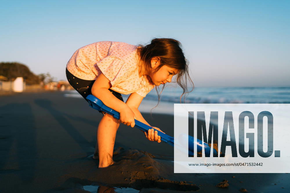 Intently focused, a young child digs in the sand with a blue shovel on the beach, with the evening light casting a soft glow on the activity Intently focused, a young child digs in the sand with a blue shovel on the beach, with the evening light casting a soft glow on the activity. High quality photo ,model released, Symbolfoto