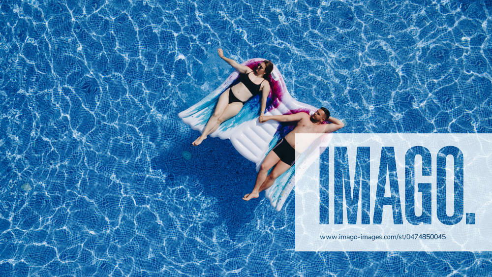 Above vertical view of people young couple taking hands with love and having fun on the blue clear swimming pool together enjoying the summer holiday vacation with trendy coloured mattress Above vertical view of people young couple taking hands with love and having fun on the blue clear swimming pool together enjoying the summer holiday vacation with trendy coloured mattress.