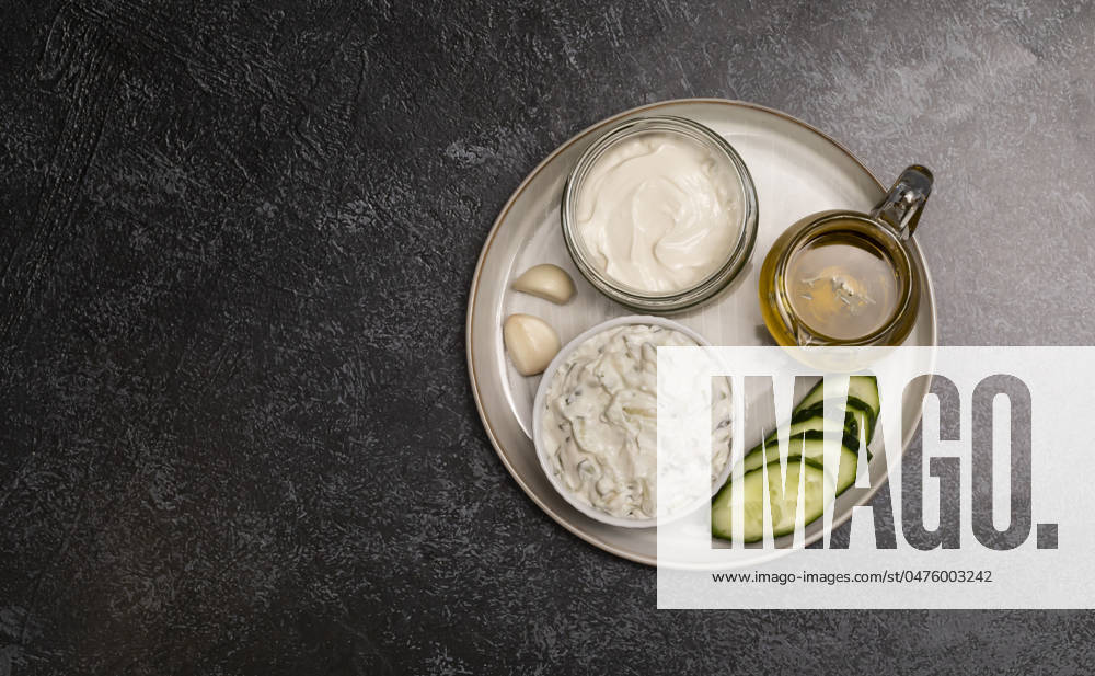 Traditional greek yogurt sauce Tzatziki,dressing in white bowl, made of grated cucumbers, sour cream yogurt,olive oil,garlic,herbs with ingredients on dark gray concrete table. Flatly, horizontal Traditional greek yogurt sauce Tzatziki in white bowl, made of chopped cucumbers, sour cream yogurt,olive oil,garlic,herbs with ingredients on on dark gray concrete table. Copyspace horizontal plane.