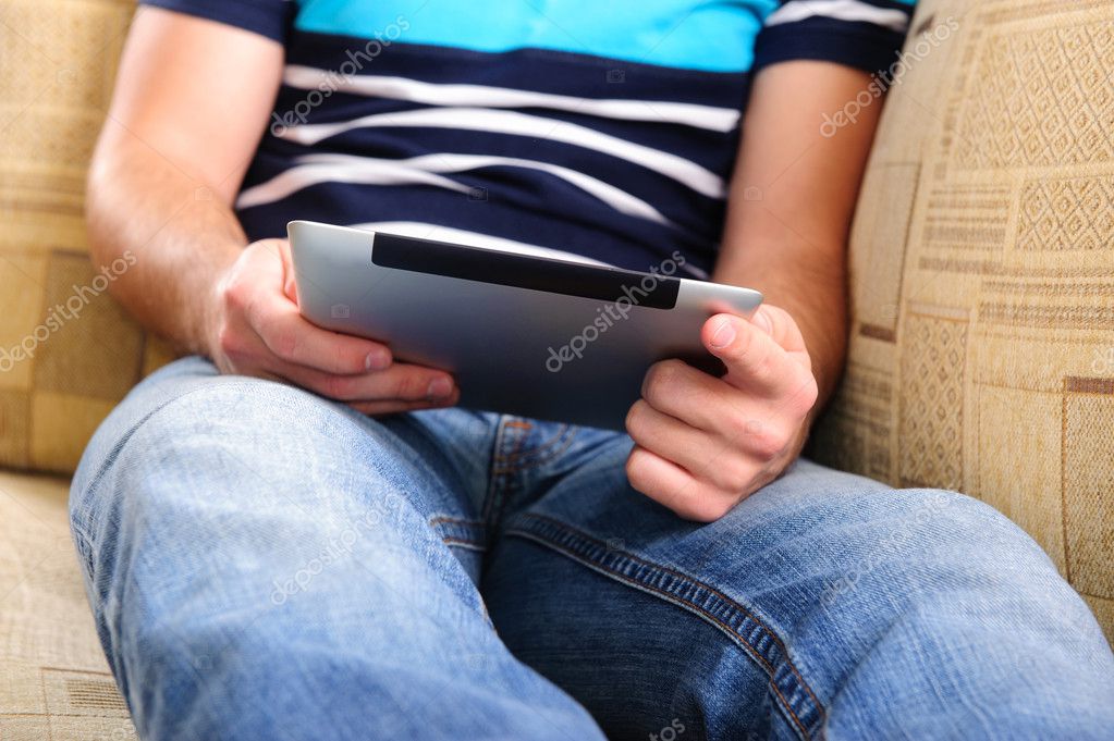 Young man using digital tablet on sofa at home model released