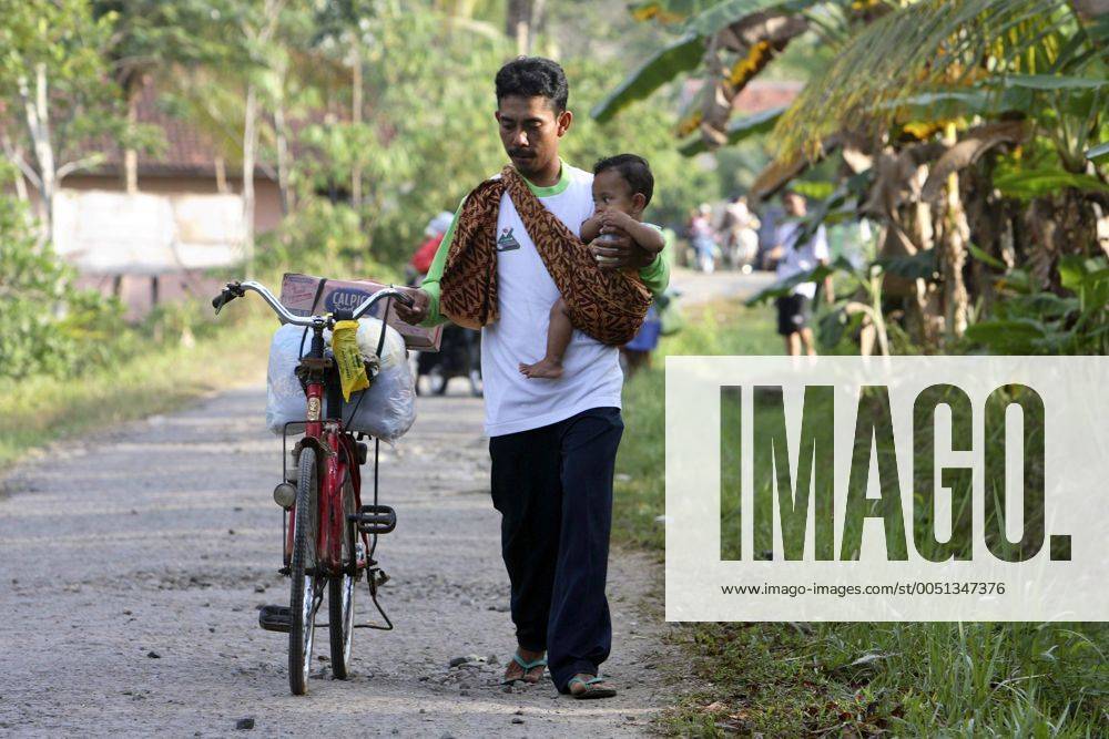 Flüchtling verlässt mit einem Baby auf dem Arm und seinem Fahrrad ein Flüchtlingslager nach dem verheerenden Tsunami in Pangandaran auf Java -