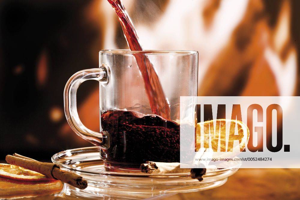 Glas Glühwein mit Zimtstangen und getrockneter Orangenscheibe vor Kaminfeuer - ibxodh00769510