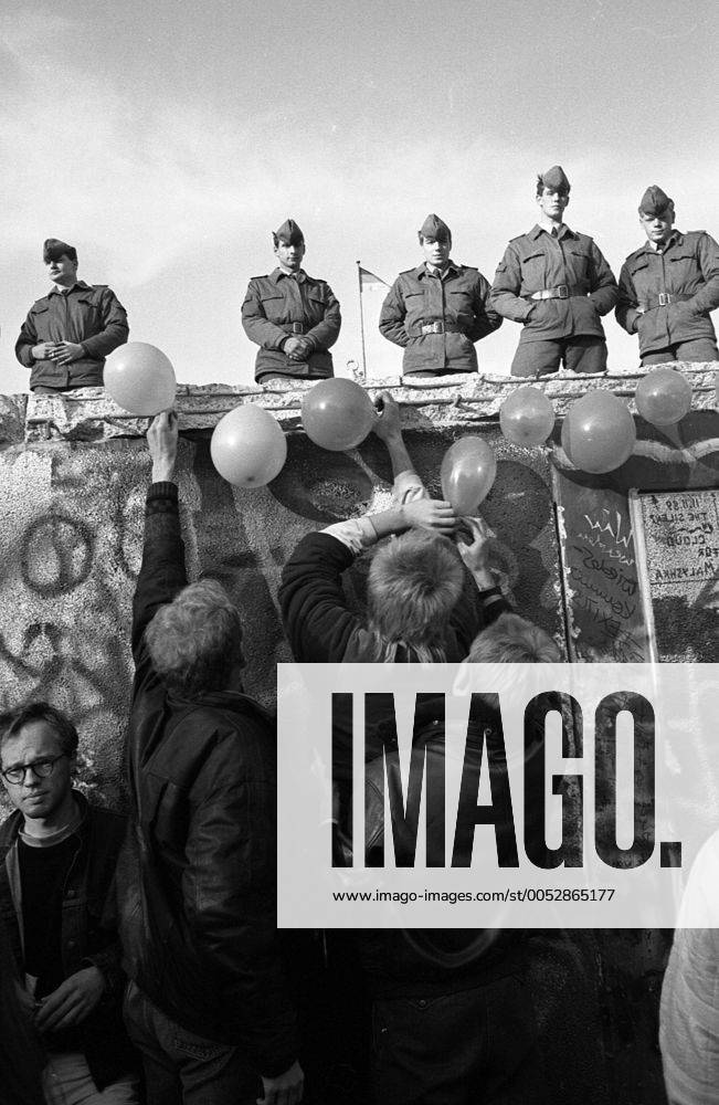 Luftballons schmücken die bereits von Mauerspechten bearbeitete Berliner Mauer unter den Augen von Volksarmisten - Mauerfall in Berlin