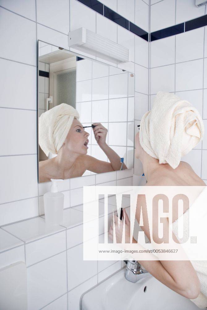 Frau beim Tuschen der Wimpern im Bad vor dem Spiegel ibxrut01448081