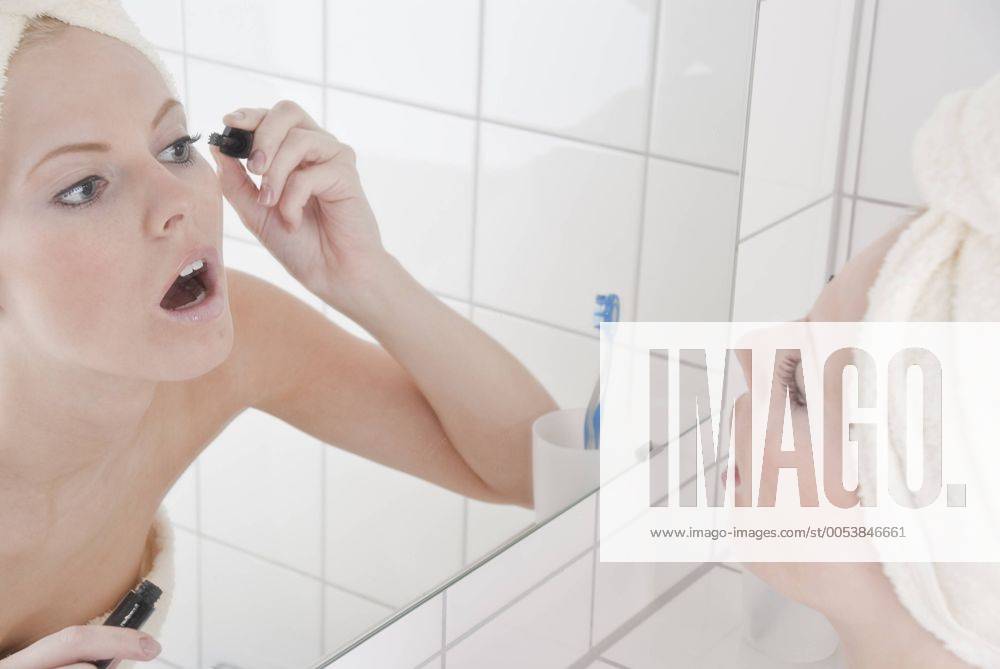 Frau beim Tuschen der Wimpern im Bad vor dem Spiegel ibxrut01448078