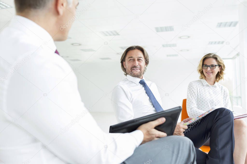 Smiling colleagues looking at businessman while sitting in new office during meeting model released
